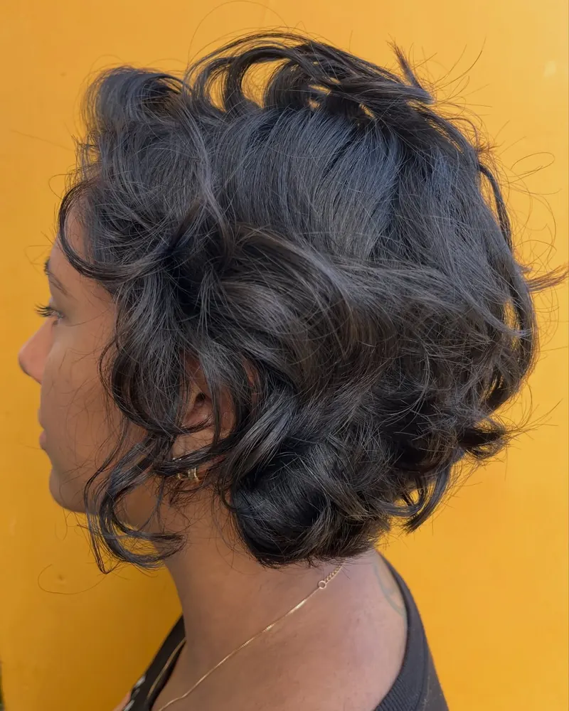 Cabelo em bob ondulado escuro, visto de perfil, com fundo de estúdio amarelo