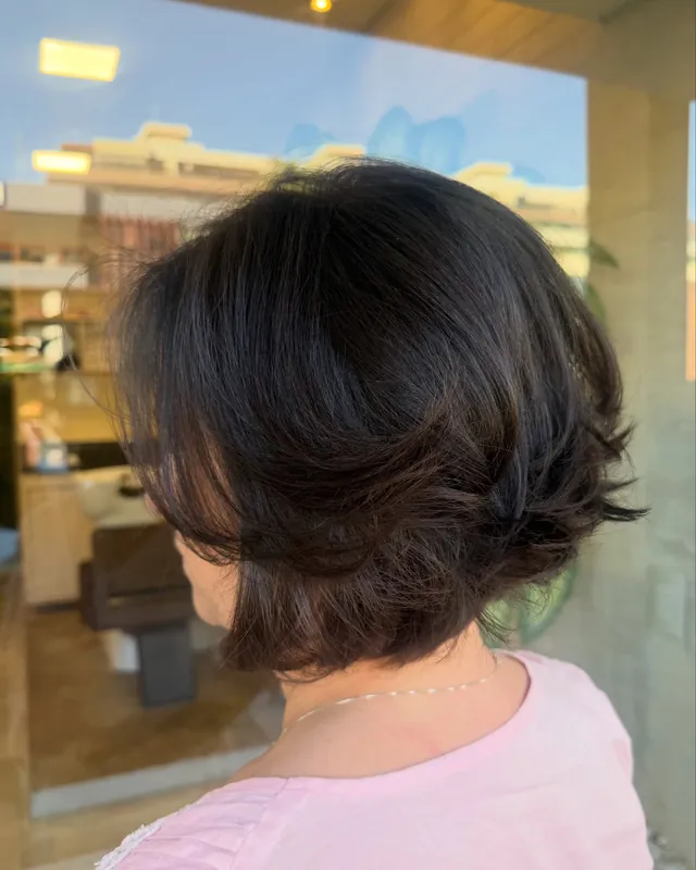 Cabelo castanho em corte bob, visto de costas, refletindo o salão ao fundo