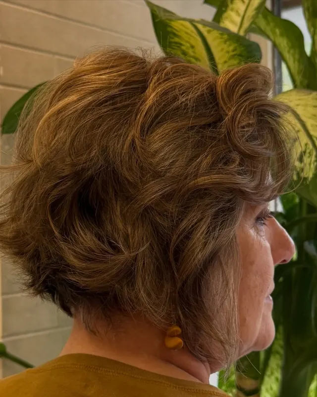 Cabelo curto ondulado castanho, visto de perfil, refletindo a rua